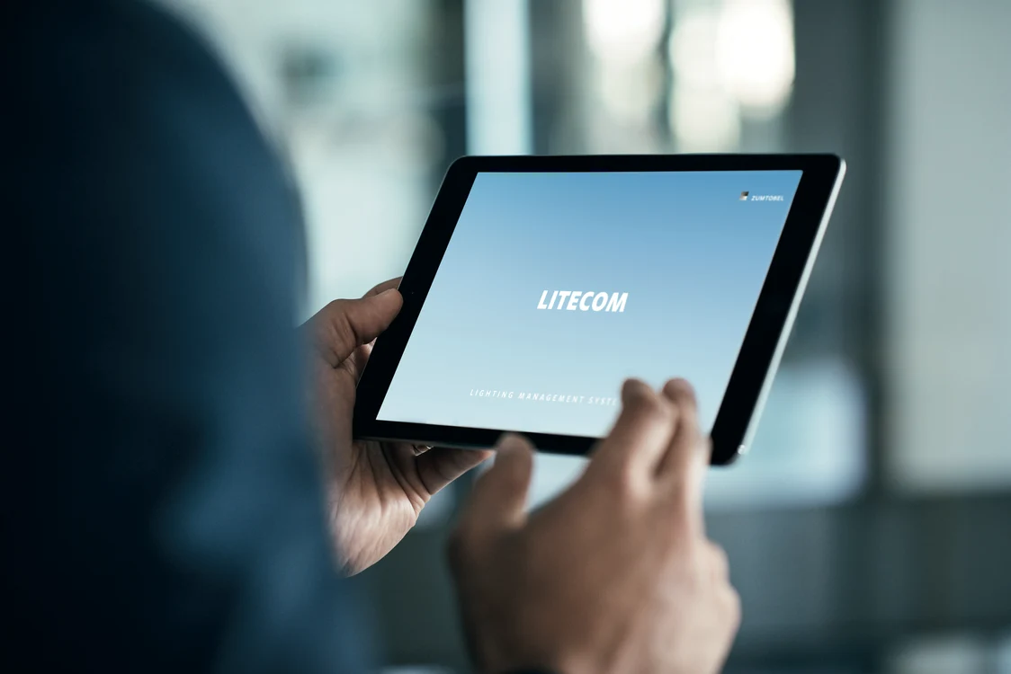 A user holds a tablet with the LITECOM lighting system in a modern office, which provides smart lighting control.