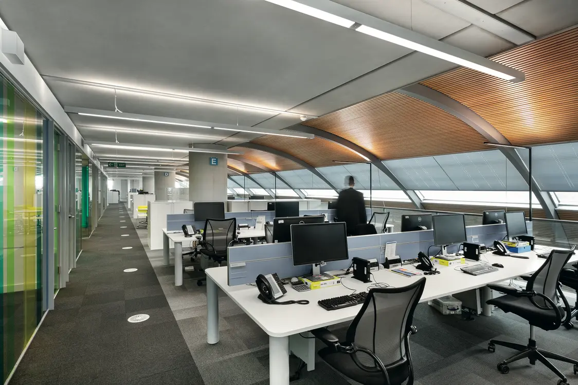 Die Kombination aus natürlichem Tageslicht durch die Fenster und gleichmäßig verteilten Deckenleuchten sorgt für eine helle, angenehme Arbeitsatmosphäre.