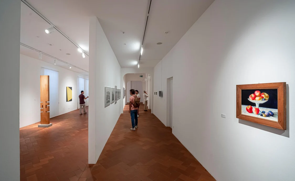 Un cono di luce diretto mette in risalto l'opera d'arte centrale sulla parete, mentre la stanza adiacente riceve un'atmosfera tranquilla grazie a un'illuminazione di base discreta.