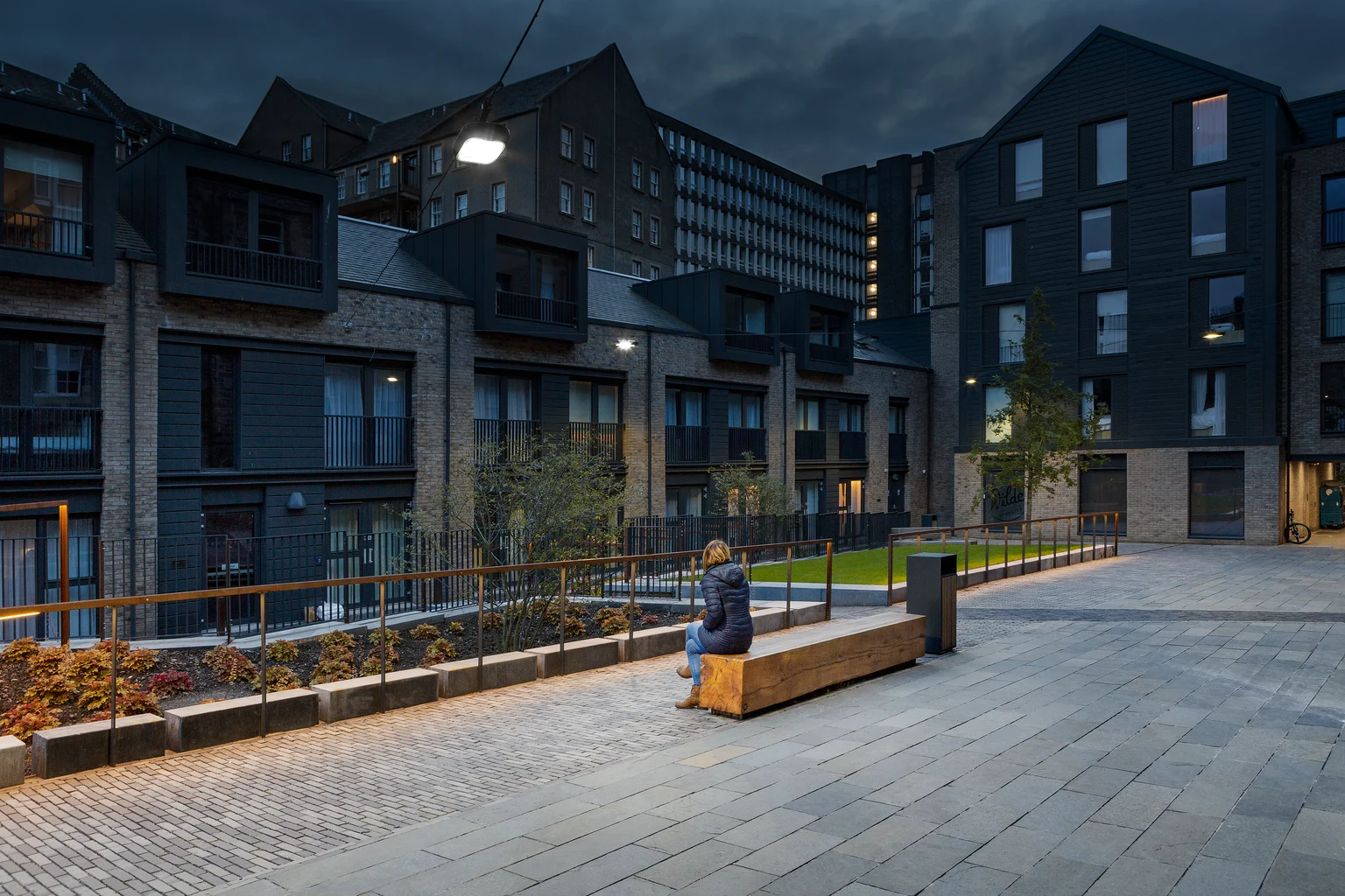 Les bancs et les espaces paysagers sont mis en valeur par un éclairage doux, créant des lieux accueillants pour se reposer et interagir socialement après la tombée de la nuit