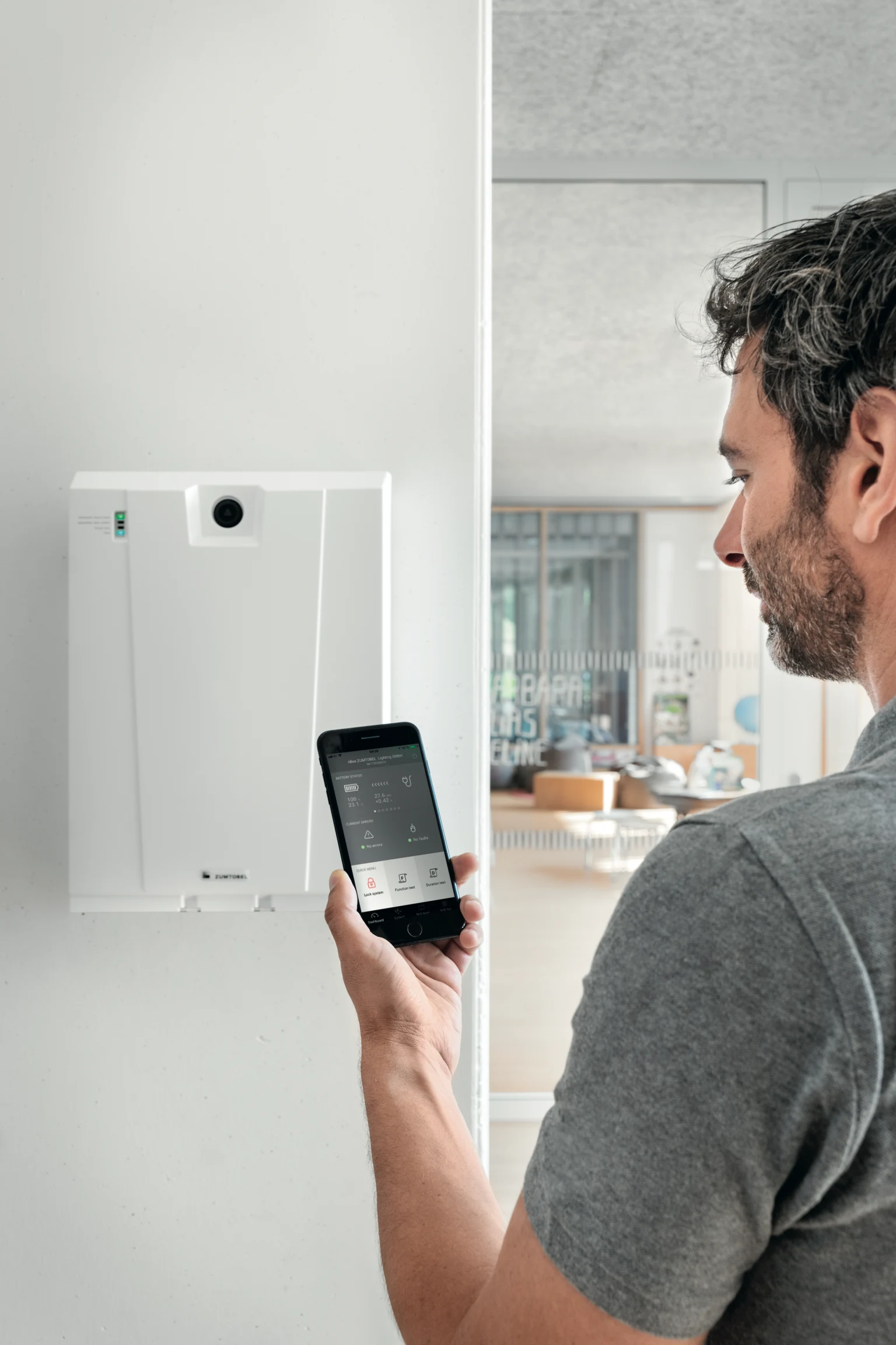 Dans un bureau moderne, un homme utilise un smartphone pour piloter le système central ONLITE nBOX ; en arrière-plan, on aperçoit une salle de réunion élégante.