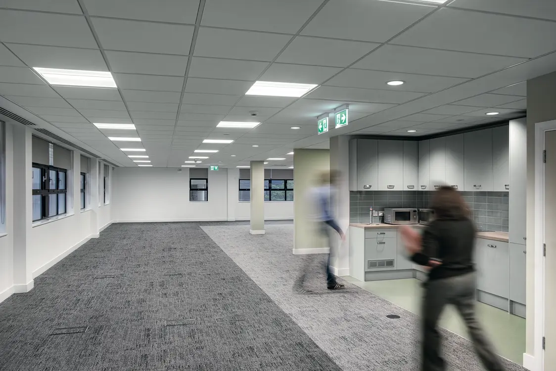 Der Raum wird durch zahlreiche Deckenleuchten sehr gleichmäßig und hell ausgeleuchtet. Tageslicht gelangt durch die Fenster an der linken Seite hinein.