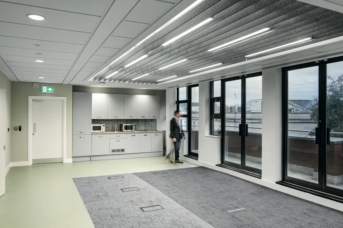 Die Decke ist mit modernen, länglichen Leuchten ausgestattet, die für eine helle und gleichmäßige Ausleuchtung sorgen. Großzügige Fenster lassen viel Tageslicht in den Raum.