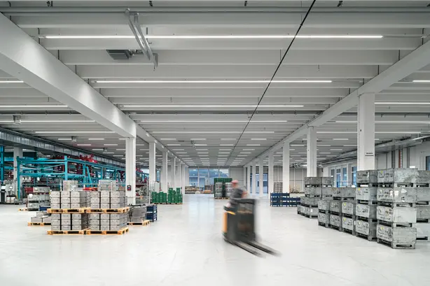 Ein Gabelstapler fährt durch ein Lagerhaus, das mit Hochregalen und gestapelten Paletten gefüllt ist.