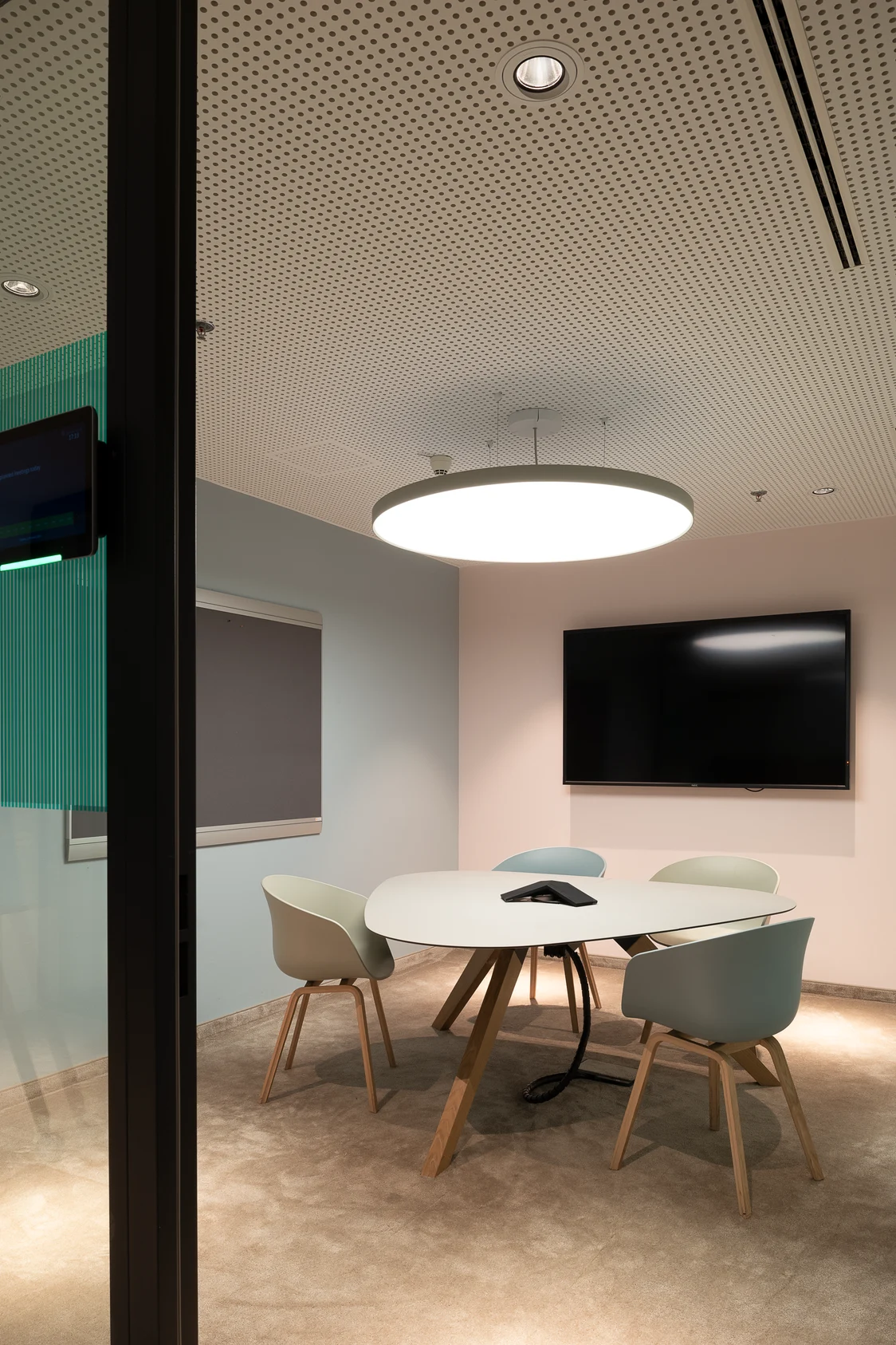 The ONDARIA II luminaire brightens a meeting room with gentle light. You can see a table, four chairs and a monitor on the wall.