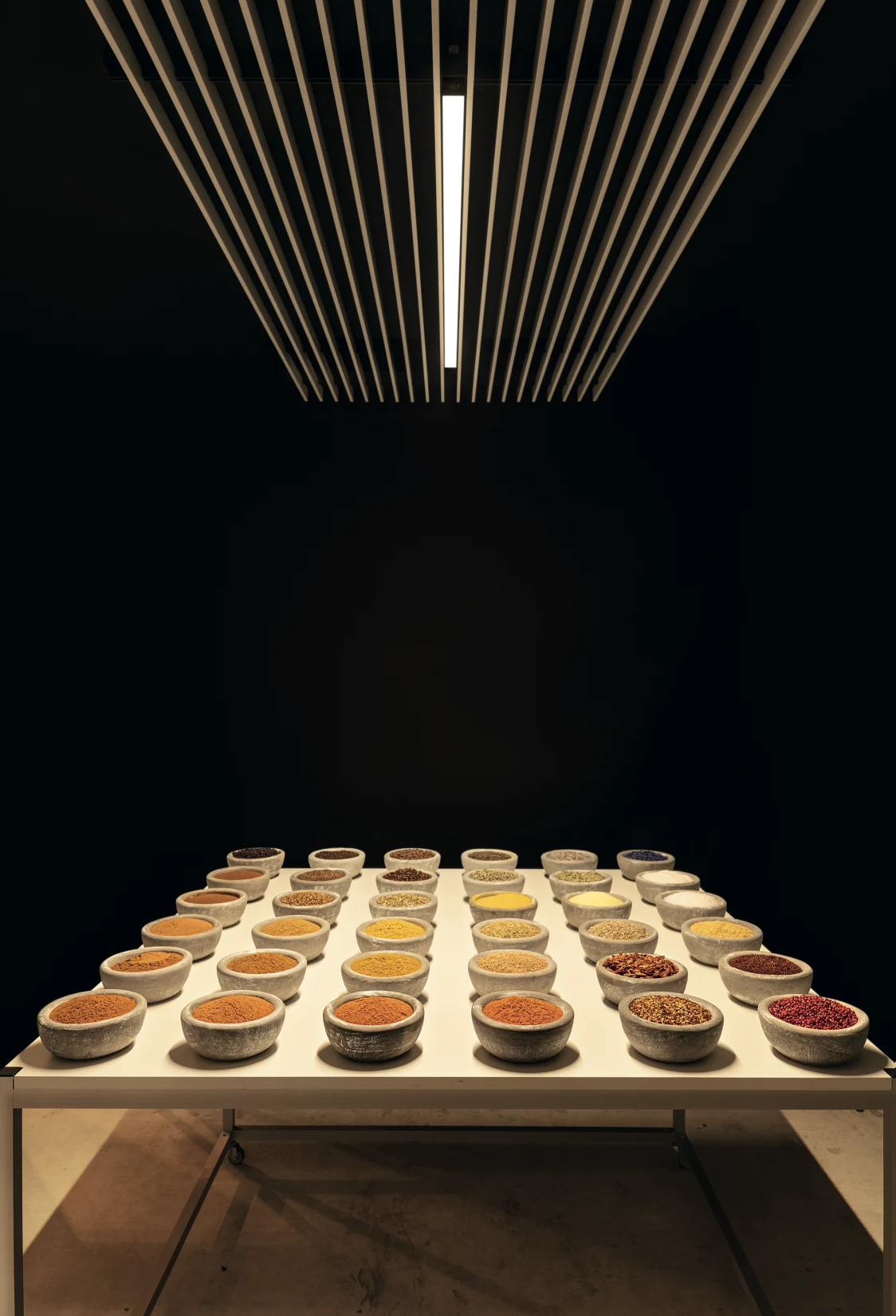 Supersystem Inline evenly illuminates a table with bowls full of spices in a dark, minimalist room.