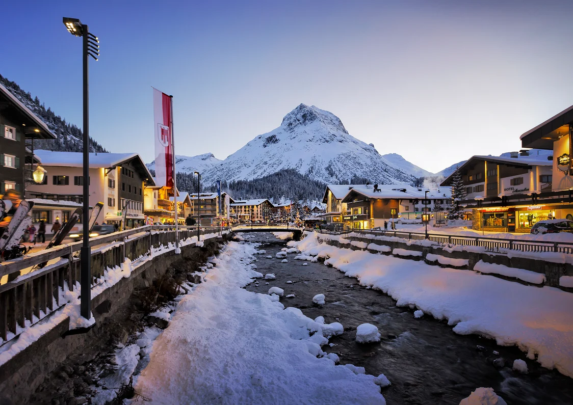 Winterliche Stadtansicht mit beleuchteten Straßen und schneebedecktem Fluss bei Sonnenuntergang Zumtobel
