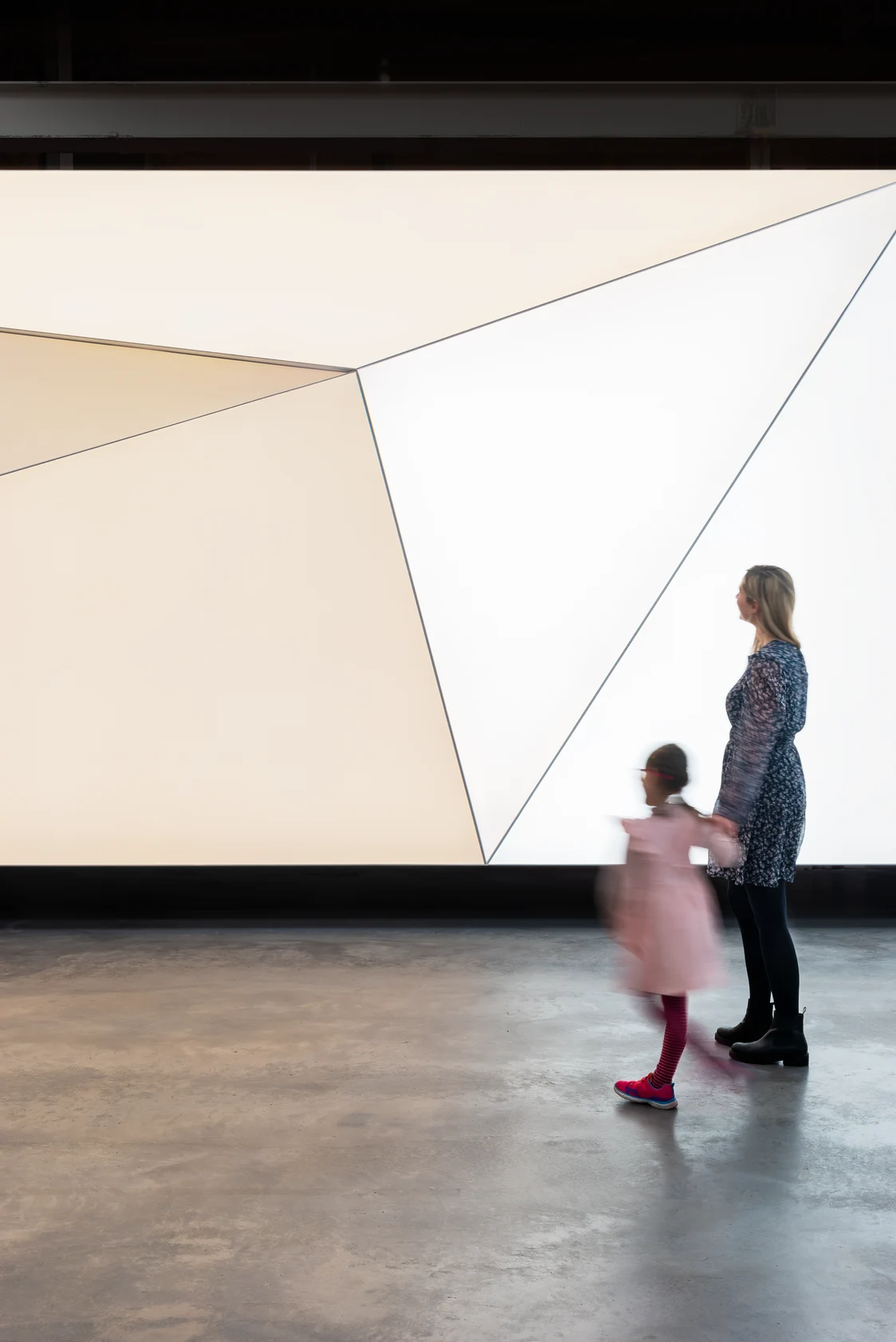 Le système d'éclairage CIELUMA crée une installation lumineuse géométrique et homogène dans un intérieur moderne, tandis que deux personnes passent à proximité.