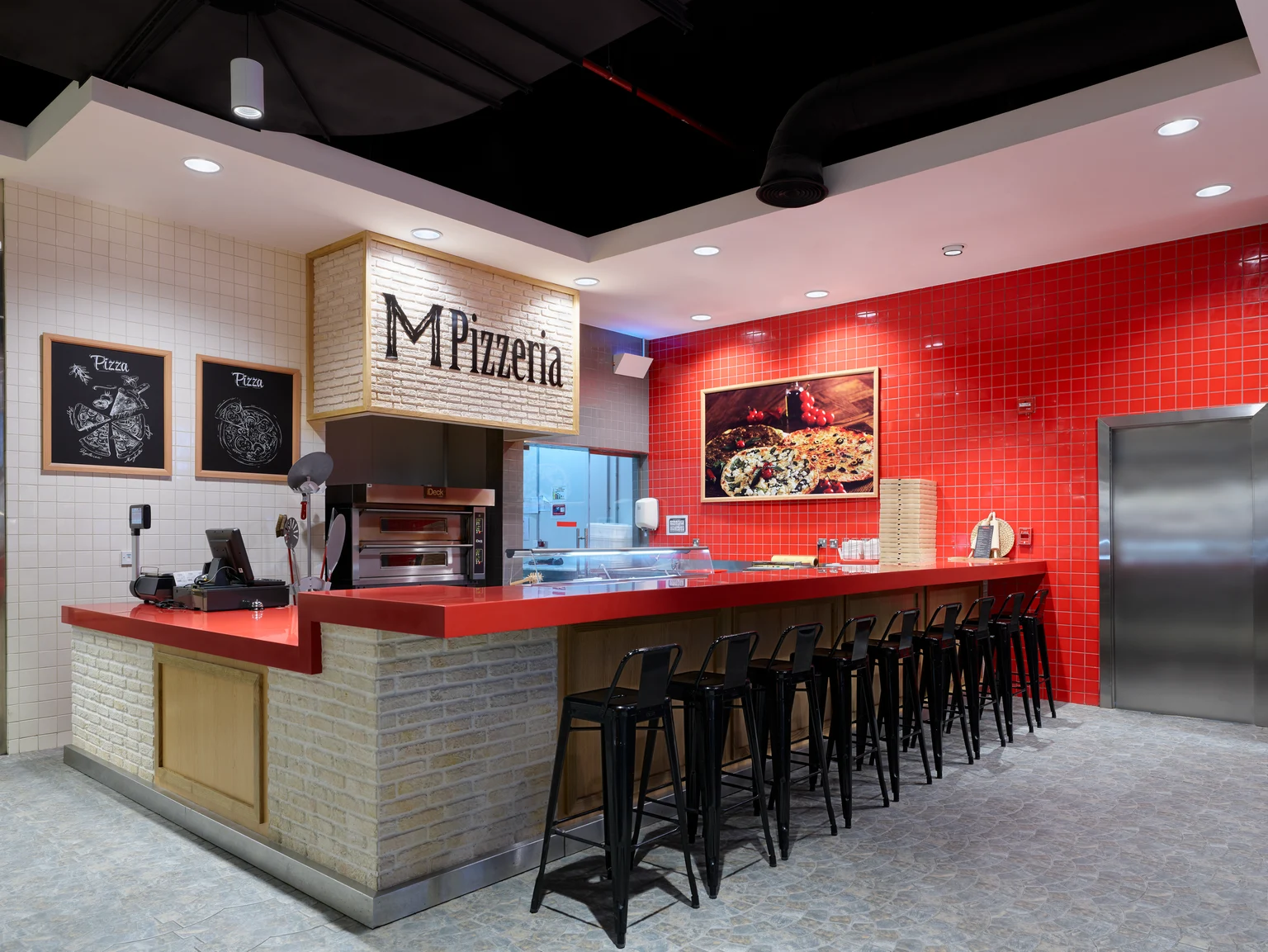 L’espace intérieur d’une pizzeria moderne avec un mur carrelé rouge, un comptoir élégant doté de tabourets de bar noirs et un espace cuisine ouvert. L’espace est bien éclairé et marie des éléments de design industriel et contemporain.
