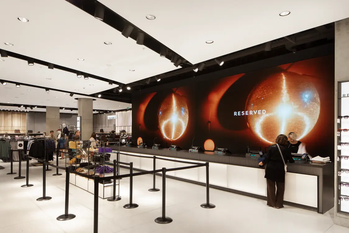 The checkout area of the fashion store features an impressive digital wall installation. The LED lighting solutions create a bright and modern atmosphere, while the clear spatial design ensures a pleasant customer experience.