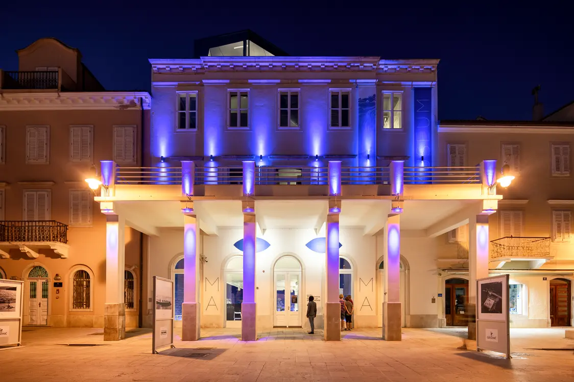 Uno spazio dal design moderno con sedute sfalsate, cuscini colorati e pareti a specchio riflettenti che creano un'atmosfera creativa. L'illuminazione crea accenti e sottolinea l'architettura dinamica della stanza.