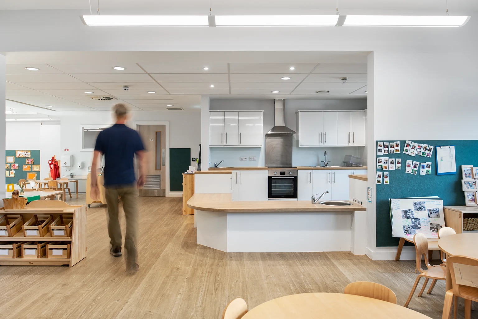 Een moderne keuken en speelruimte voor een kinderdagverblijf, met warme houten vloeren, heldere verlichting en een open ontwerp, ter bevordering van een uitnodigende en functionele educatieve ruimte.