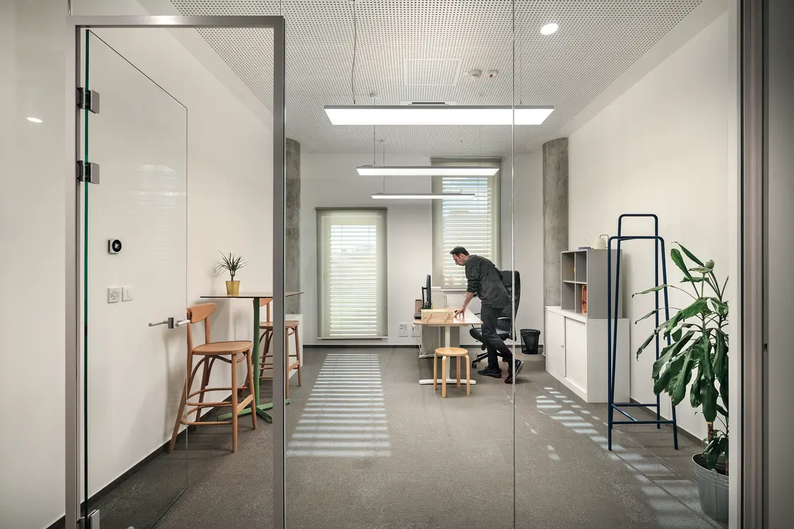 Un ufficio luminoso e minimalista con mobili moderni in legno e ampie superfici vetrate. Una persona lavora alla scrivania, mentre le piante conferiscono allo spazio un'atmosfera accogliente.