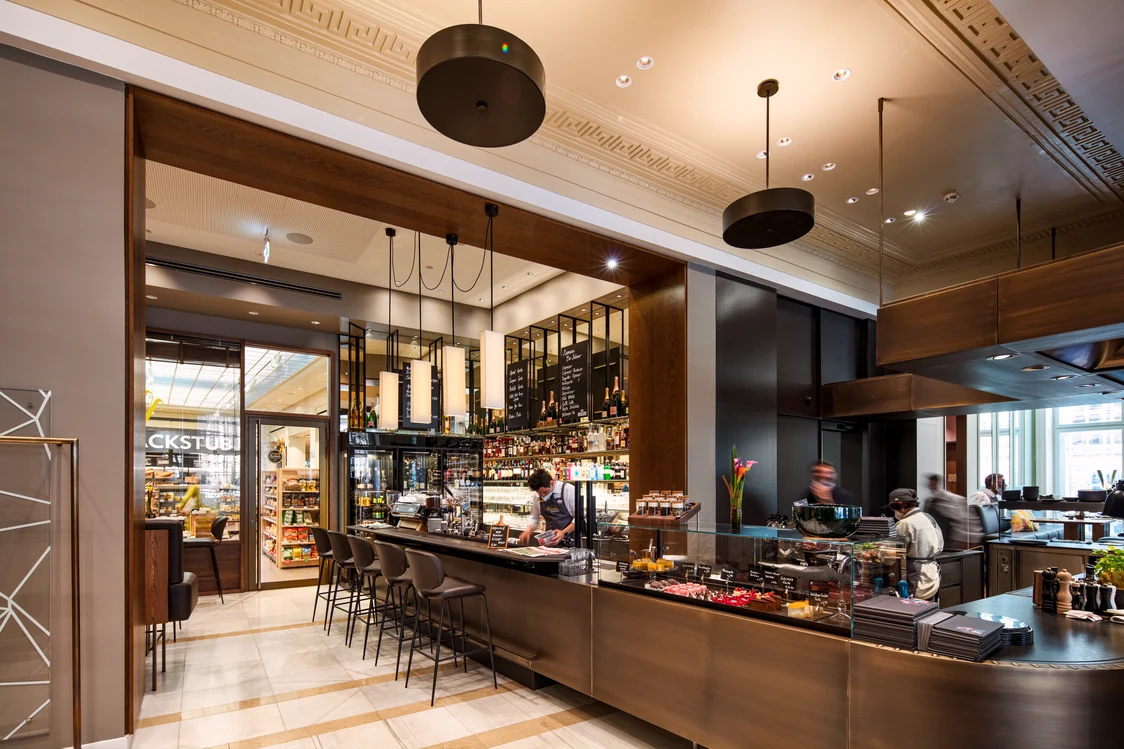 Modern café in the Haus am Schottentor with a stylish bar, elegant furnishings, and accentuated lighting design. The lighting creates an inviting atmosphere and highlights the high-quality interior architecture.