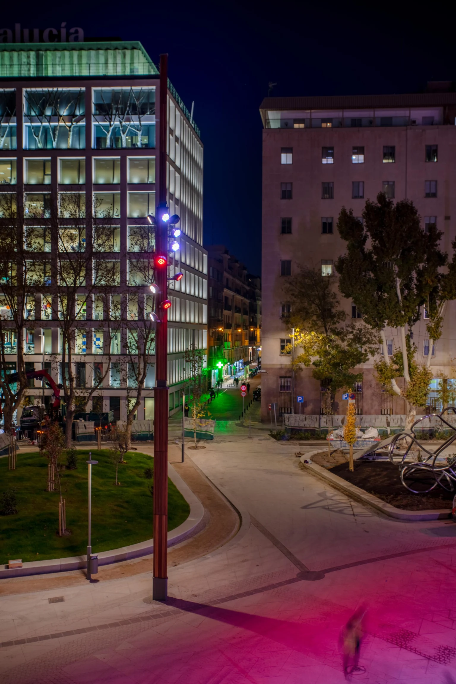 De combinatie van rode en witte verlichting op de mast zorgt voor visueel opvallende effecten, terwijl gekleurde lichtprojecties op de grond bijdragen aan een levendige en uitnodigende sfeer in de openbare ruimte.