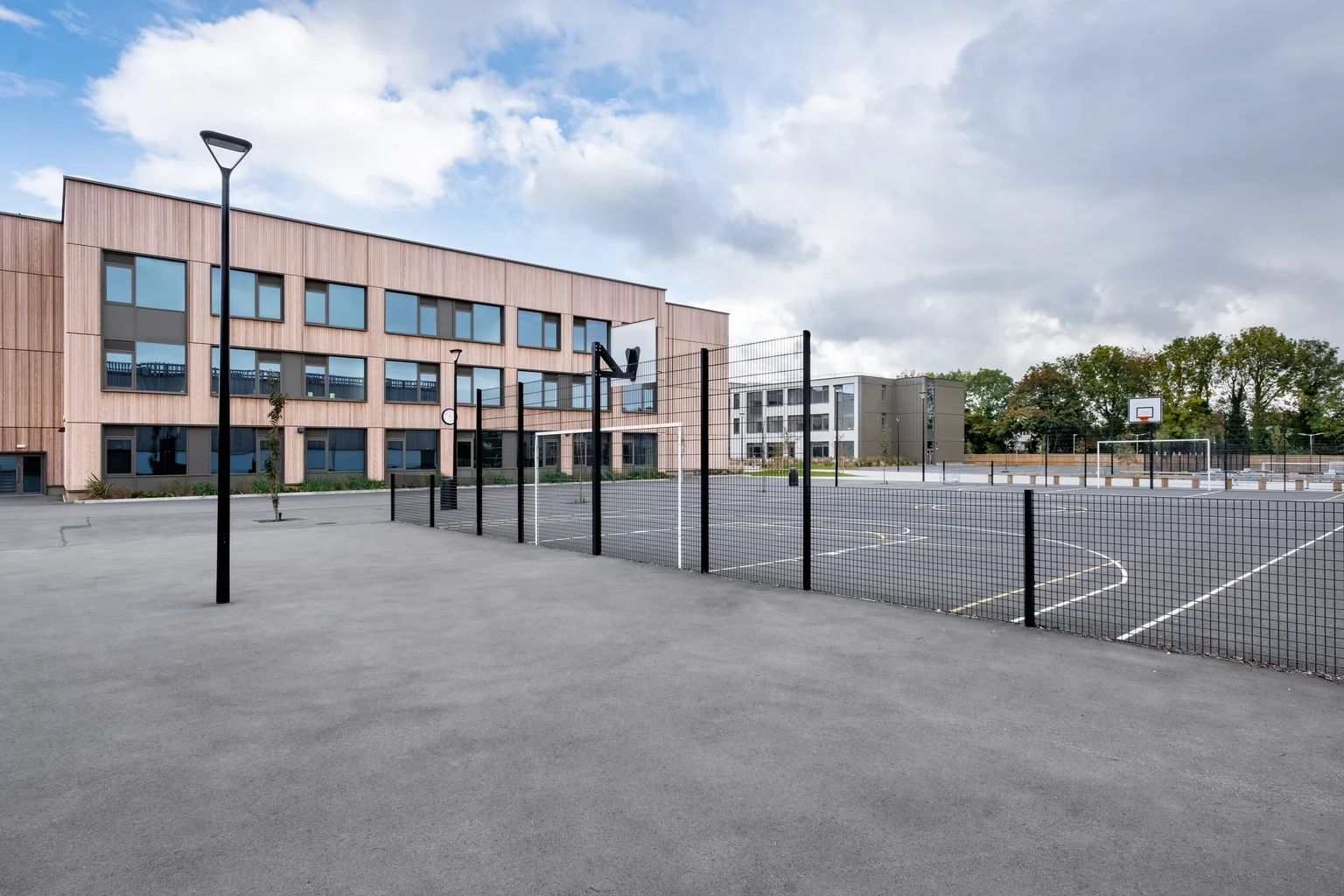 Una facciata moderna in legno con un disegno artistico, accompagnata da una passerella pavimentata, rastrelliere per biciclette e un lampione esterno. L'ambientazione riflette un design architettonico sostenibile e funzionale.