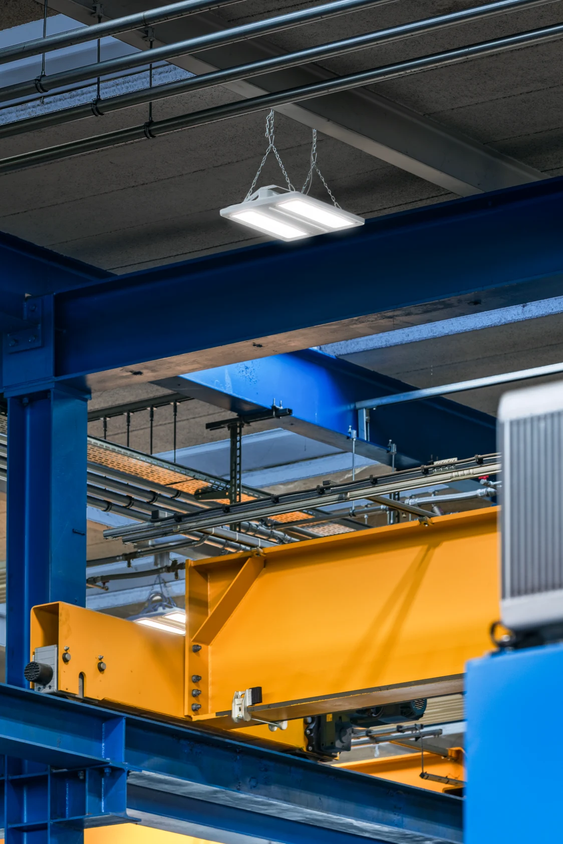 Industriehalle mit gelbem Brückenkran, blauen Stahlträgern und moderner LED-Beleuchtung. Die robuste Konstruktion und klare Beleuchtung unterstützen sichere und effiziente Arbeitsabläufe.