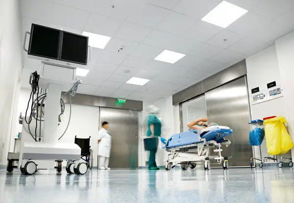 A hospital corridor with NHS workers at the lift with a patient trolley