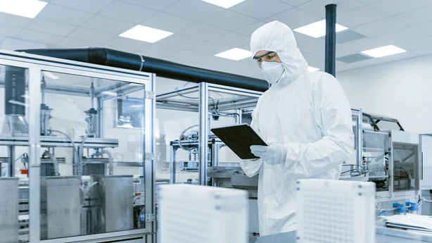 Ein Steriler Raum in einem pharmazeutischen Betrieb mit einer Person im Schutzanzug. Im Hintergrund sind die Reinraum Leuchten von Zumtobel zu sehen.