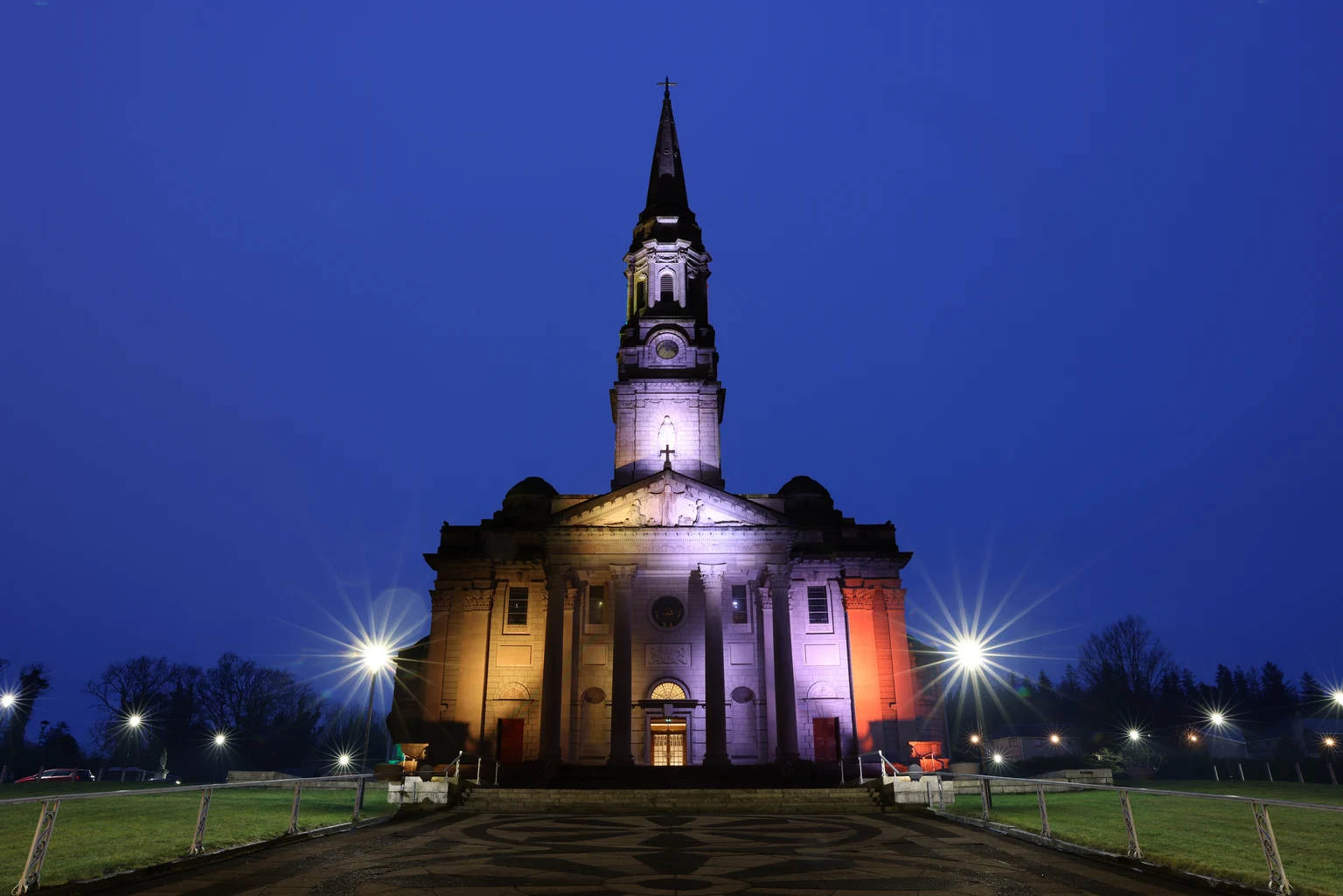 Dynamische buitenverlichting baadt de kerkgevel in levendige kleuren, waardoor het gebouw 's nachts een opvallend herkenningspunt wordt en verschillende lichtsferen mogelijk zijn, afhankelijk van de gelegenheid.
