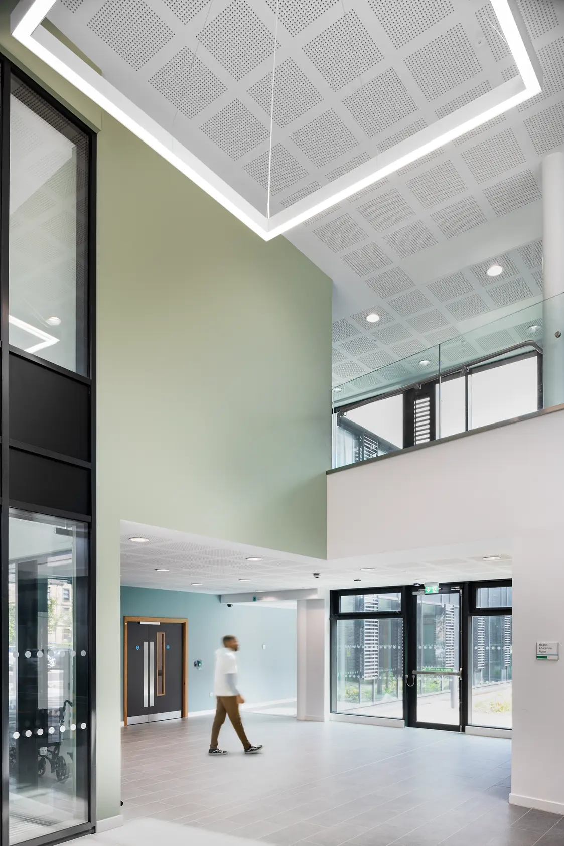 A bright entrance area with large glass facades and a high ceiling. A square LED light panel hangs centrally, complemented by integrated LED spotlights that evenly illuminate the room.