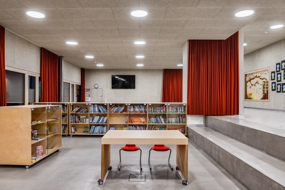  Een moderne, minimalistische ruimte met boekenplanken, rode gordijnen en een tafel met twee stoelen. De ruimte wordt verlicht door heldere plafondlampen.