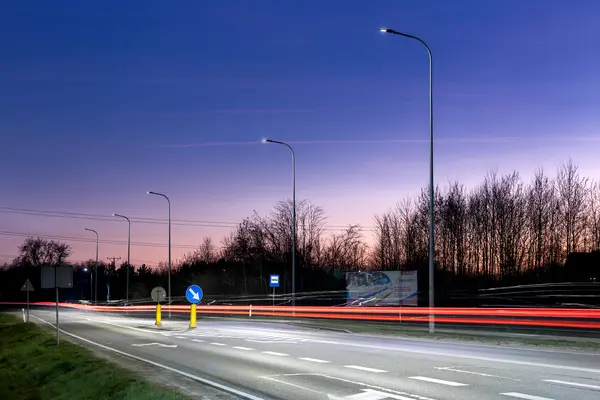 A road in Wejherowo at dusk with trees in the distance and a lighting column for safety