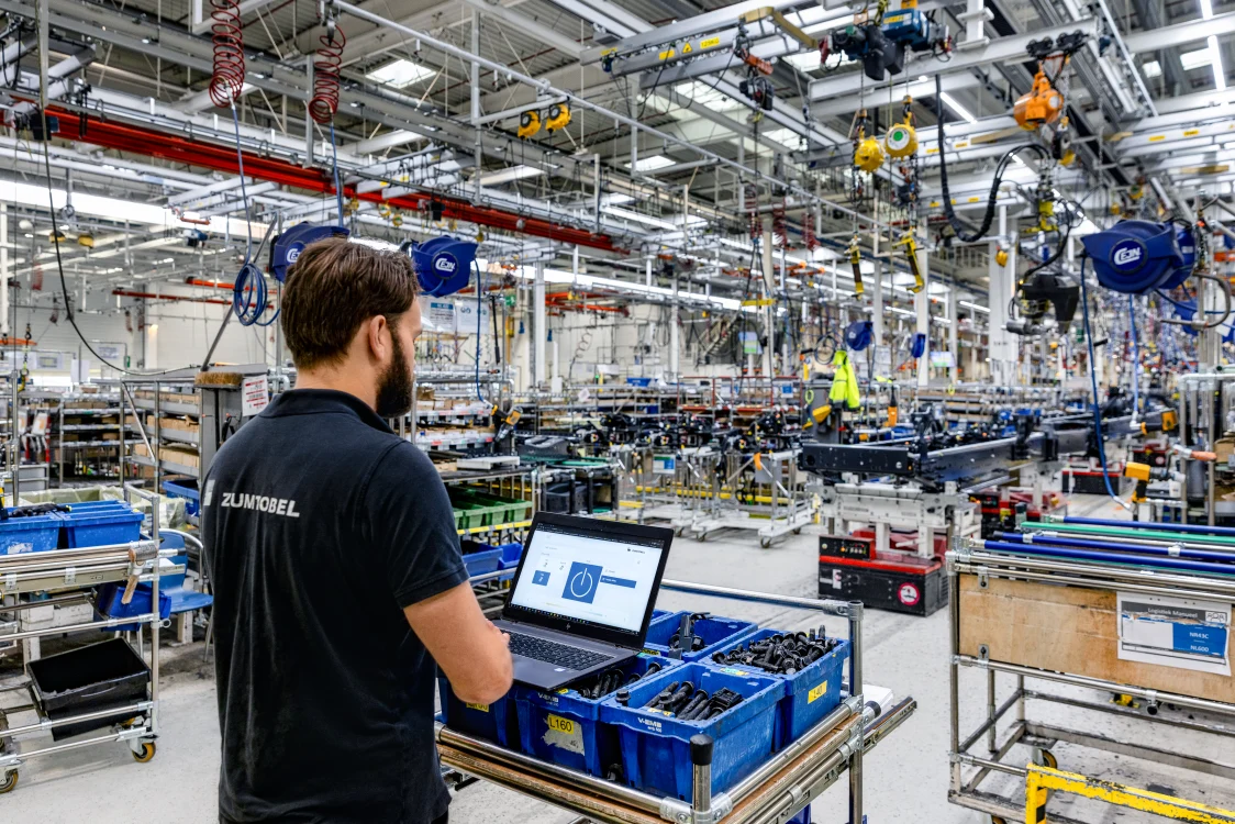 Techniker in Industriehalle bei der Wartung eines Beleuchtungssystems – Arbeiten am Laptop zur Sicherstellung langfristiger Effizienz und Zuverlässigkeit.