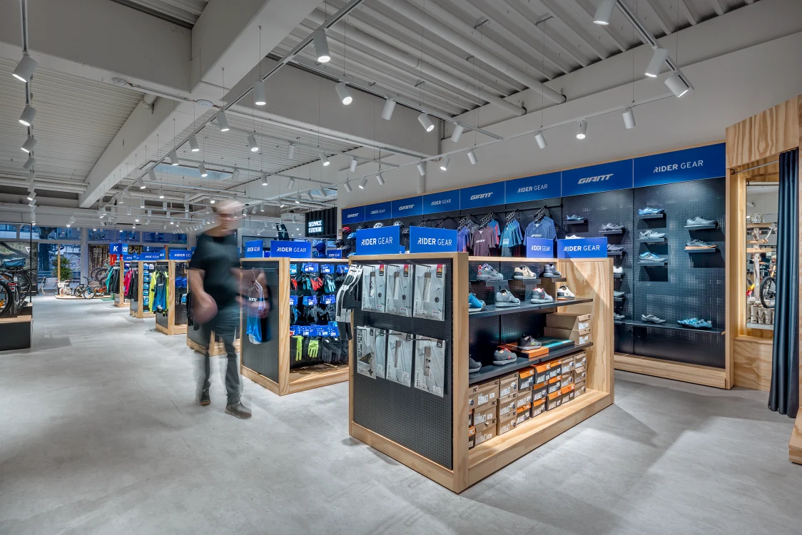 Fahrradshowroom mit mehreren ausgestellten Fahrrädern und einem Kunden beim Probefahren, die Lichtlösung mit Deckenstrahlern hebt die Produkte hervor und schafft eine angenehme Einkaufsatmosphäre.