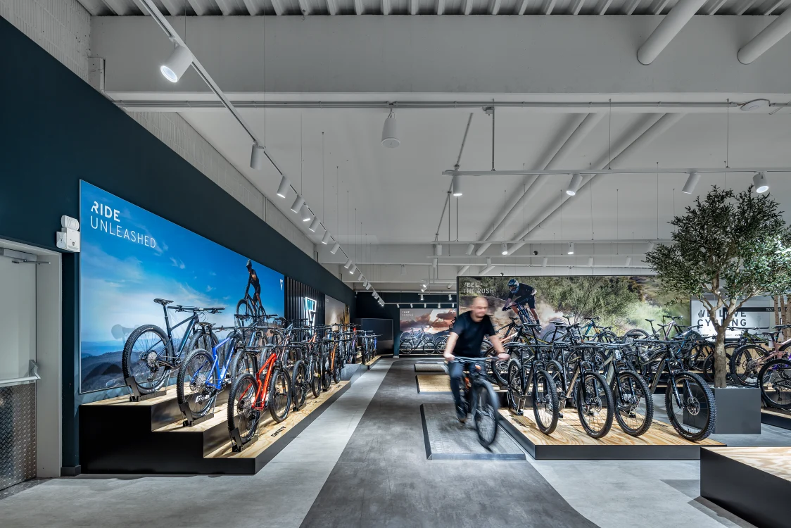 Verkaufsfläche mit Regalen für Fahrradzubehör und Bekleidung, die Lichtlösung mit Spots an der Decke sorgt für eine klare, gut ausgeleuchtete Warenpräsentation.