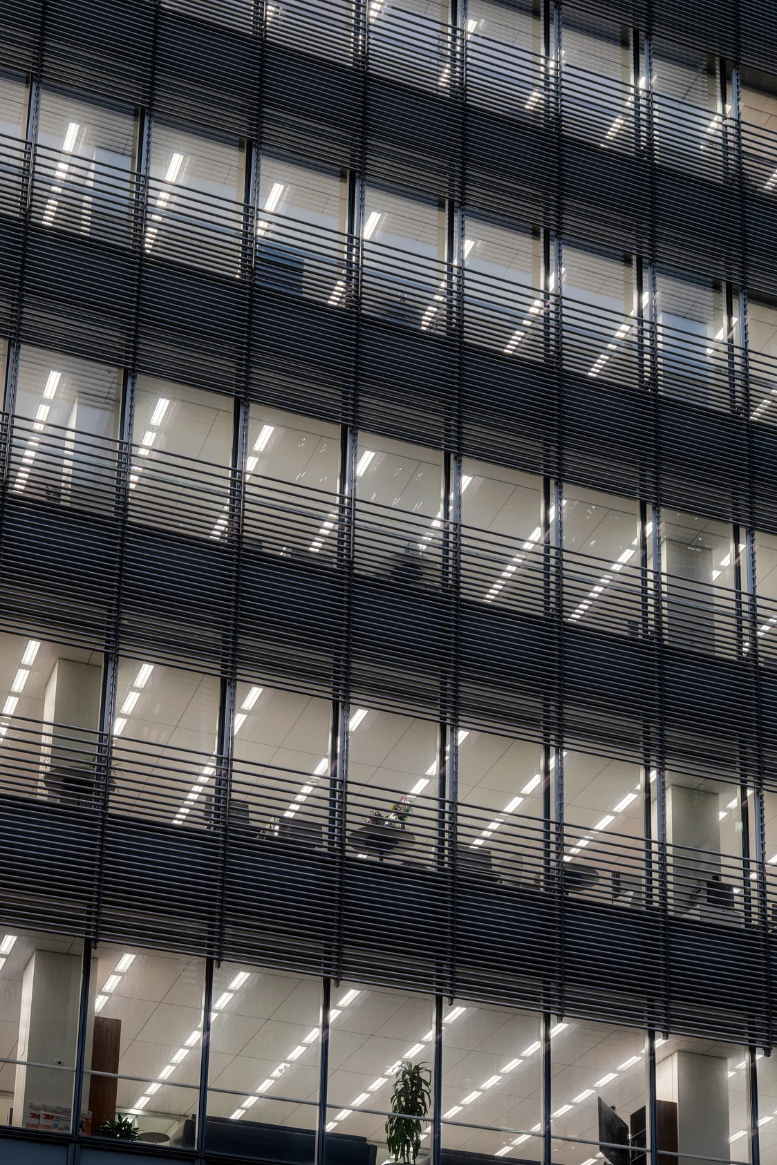 Ein Bürogebäude mit modernen LED-Leuchten, die durch die Fenster sichtbar sind und eine gleichmäßige Ausleuchtung der Arbeitsbereiche gewährleisten.
