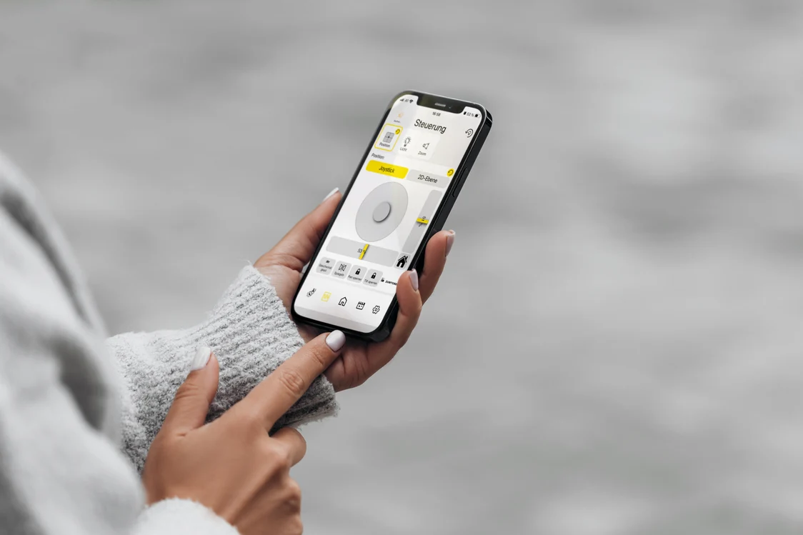 Une personne pilote le système AGILIO via un smartphone affichant l’interface de contrôle.