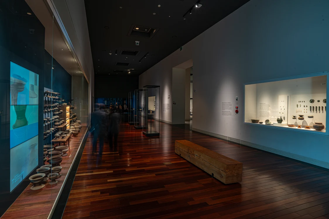 Museum corridor with illuminated display cases on the walls showcasing various ceramics and artifacts; the lighting solution highlights the exhibits and creates a pleasant atmosphere on the wooden flooring.