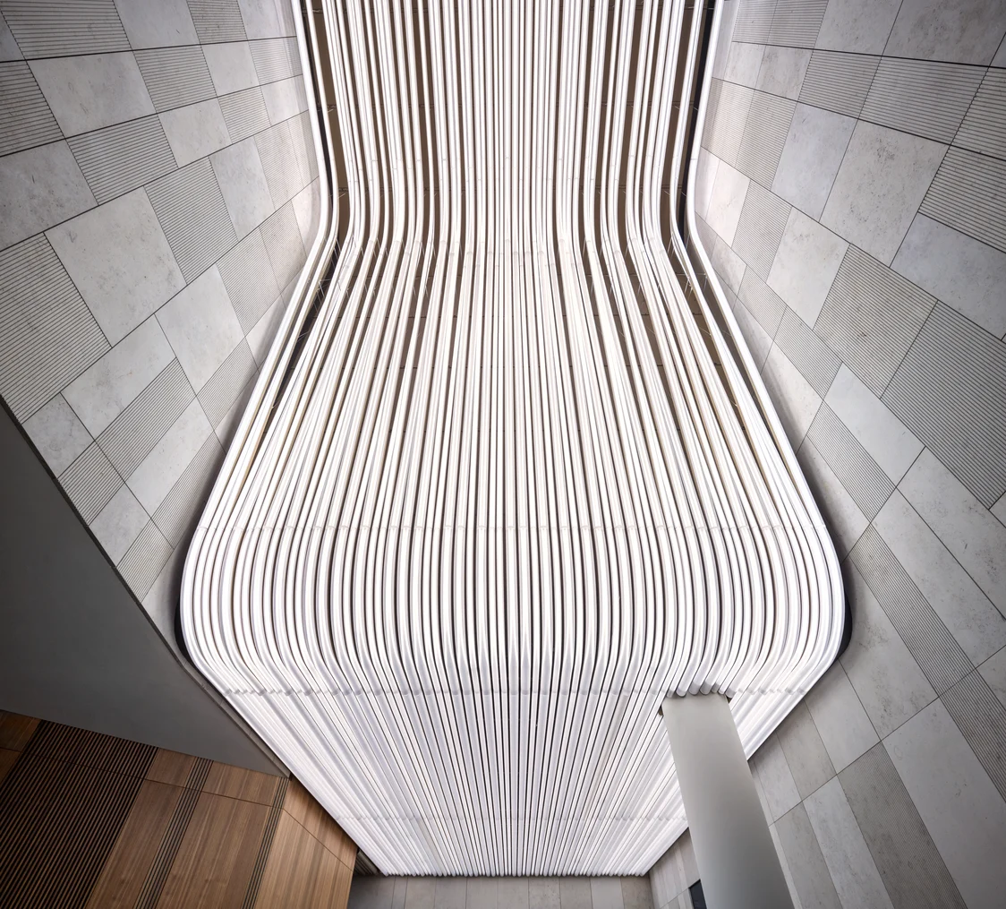 Un gratte-ciel moderne aux lignes illuminées se dresse dans un paysage urbain, entouré d’autres bâtiments de bureaux. Une ligne de lumière verticale court le long de l’angle vitré, affirmant l’identité visuelle du bâtiment une fois la nuit tombée.