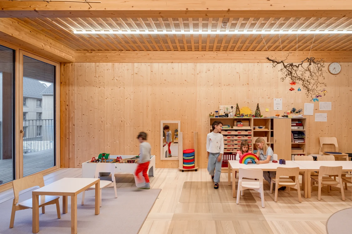 Speelruimte in het kindertehuis met houten bekleding, kindvriendelijke inrichting en gelijkmatige led-plafondverlichting. De verlichtingsoplossing zorgt voor een rustige, veilige sfeer en ondersteunt activiteiten zoals spelen, knutselen en leren