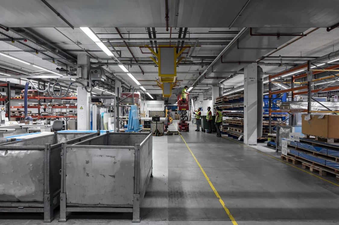 Hall de production avec éclairage industriel Zumtobel, machines et ouvriers sous lumière réfléchissante, Zumtobel