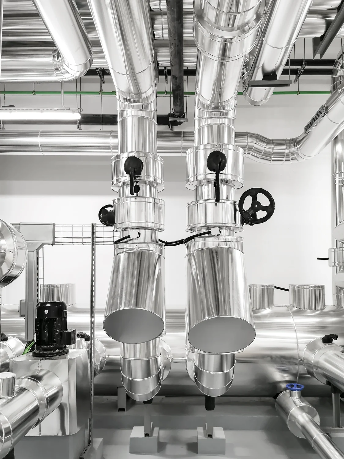 Eine hochmoderne EXTONA Beleuchtung illuminiert eine technische Anlage mit glänzenden Metallrohren in einem sterilen industriellen Umfeld.