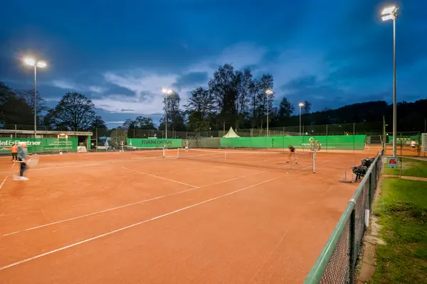 Tennis court being illuminated at night with Tennis players mid shot