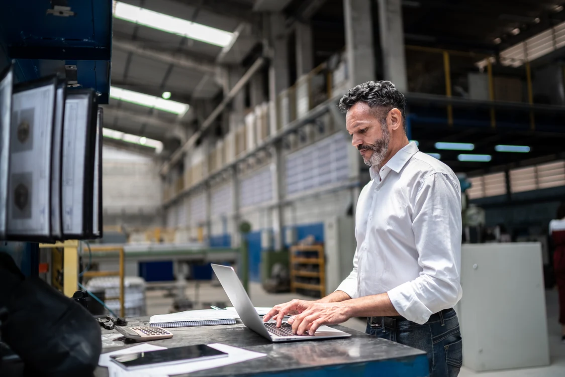 A technician in an industrial hall works on a computer - precise implementation of a lighting solution within the framework of professional project management.