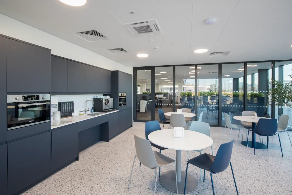 MEMS power Generation Headquarters, Gillingham - Modern meeting room featuring a large conference table surrounded by upholstered chairs, with a wall-mounted display screen and integrated shelving. Floor-to-ceiling glazed partitions provide views across the office and allow natural light to fill the contemporary workspace