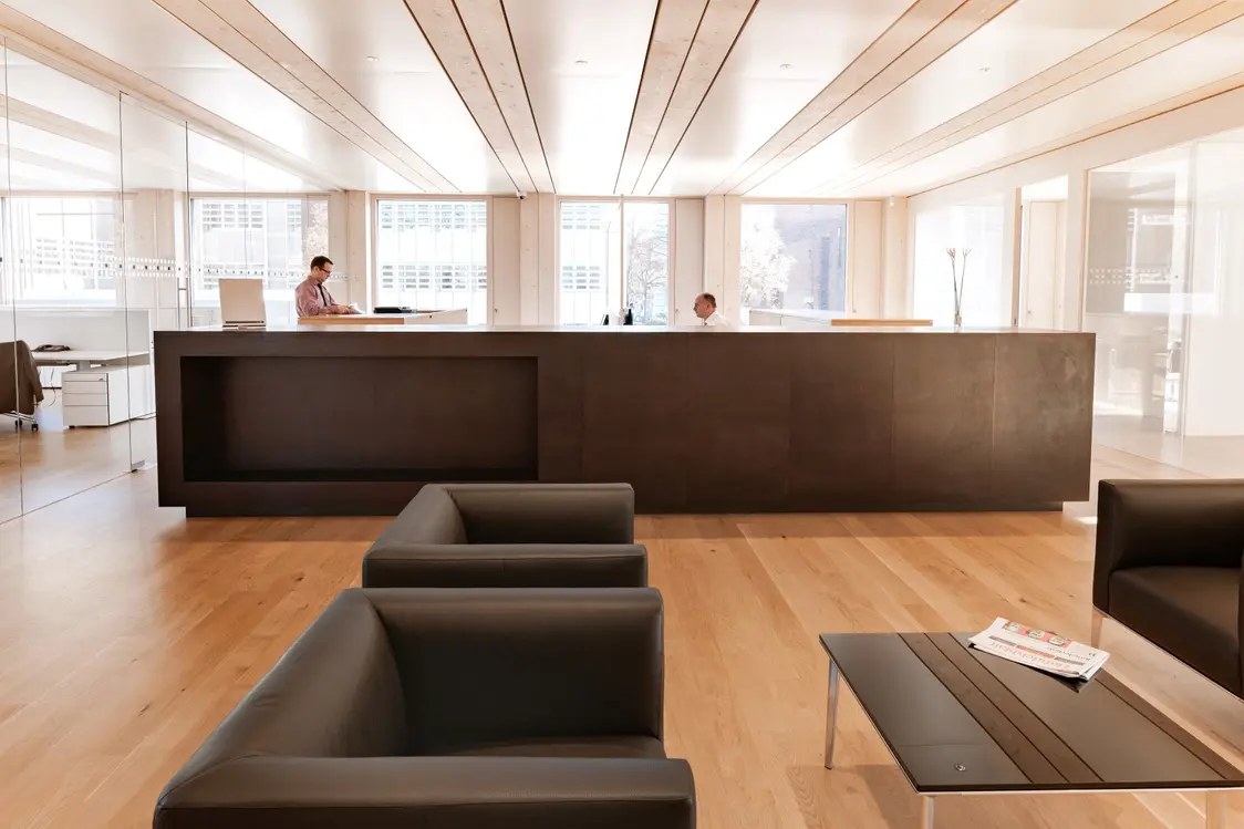 Luminosa area reception con ampio bancone e posti a sedere, inondata di luce diurna che filtra attraverso le ampie finestre. L'illuminazione a soffitto è discreta e contribuisce a un'atmosfera piacevole e inondata di luce nella stanza.
