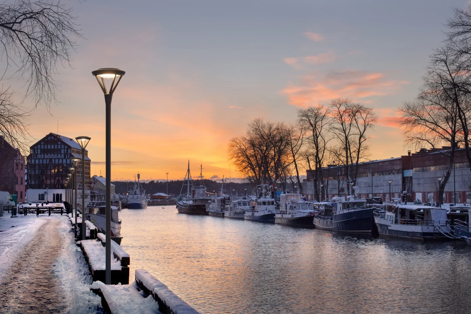 Hafen bei Sonnenuntergang mit beleuchteten Straßenlaternen und Booten im Wasser, Zumtobel