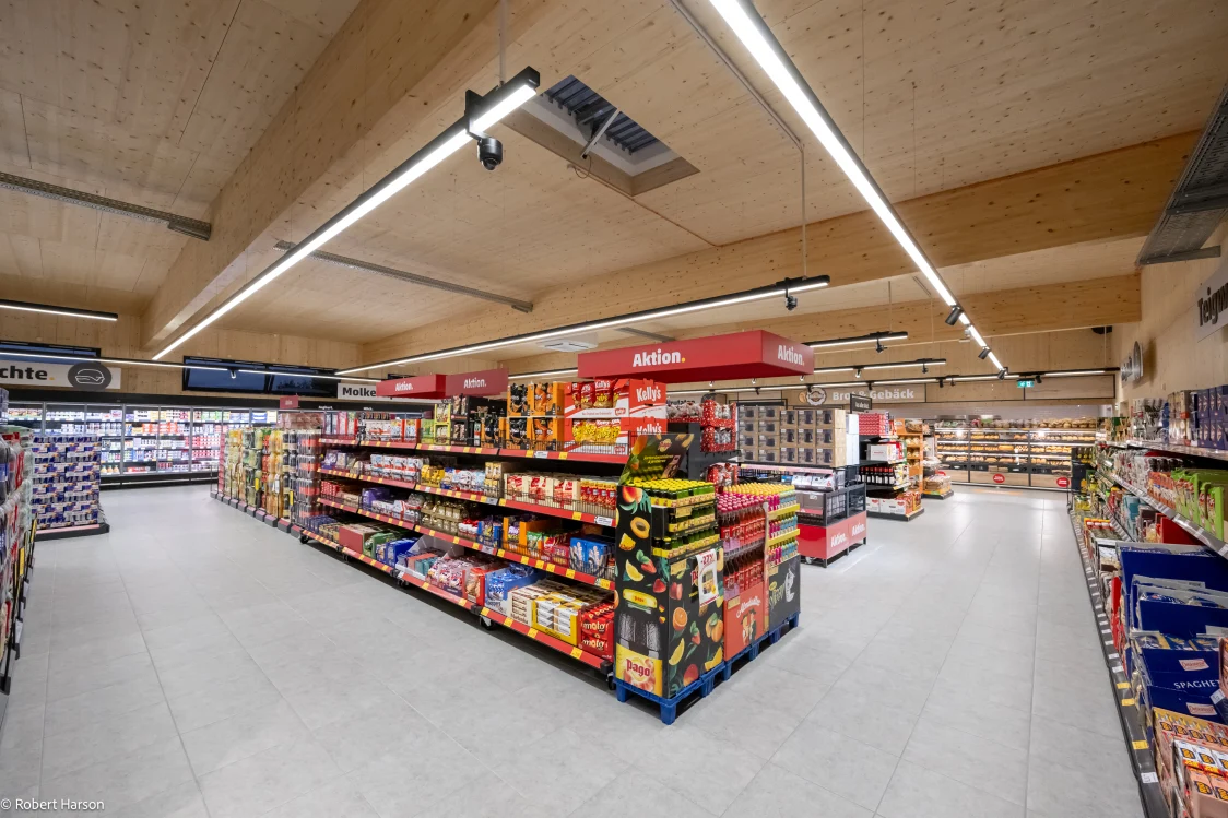 Interior view of the sustainable PENNY store in Weiden am See with wooden ceiling, energy-efficient LED lighting system TECTON II, and well-stocked shelves.