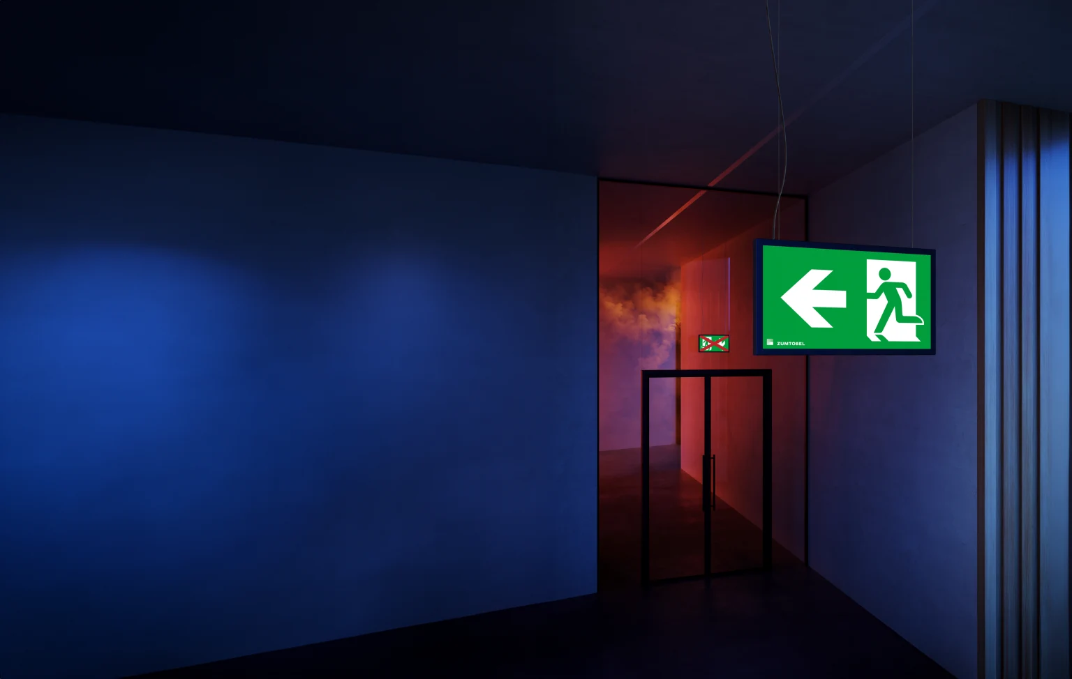 Luminaire de sortie de secours SMARTSIGN de Zumtobel dans un couloir sombre avec une fumée rougeâtre montante ; à l'arrière-plan, un second luminaire sur une porte en verre indique la voie d'évacuation sûre en cas d'incendie.