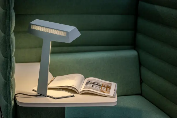 Le luminaire de bureau TALuna est placé devant un canapé vert.
