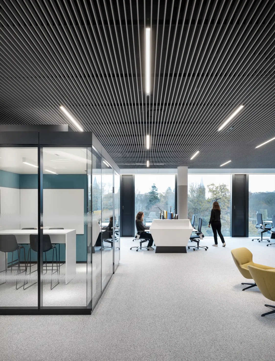 Open-plan office at Continental headquarters featuring SUPERSYSTEM inline lighting, acoustic slatted ceiling, glass meeting pod, and modern ergonomic workstations.