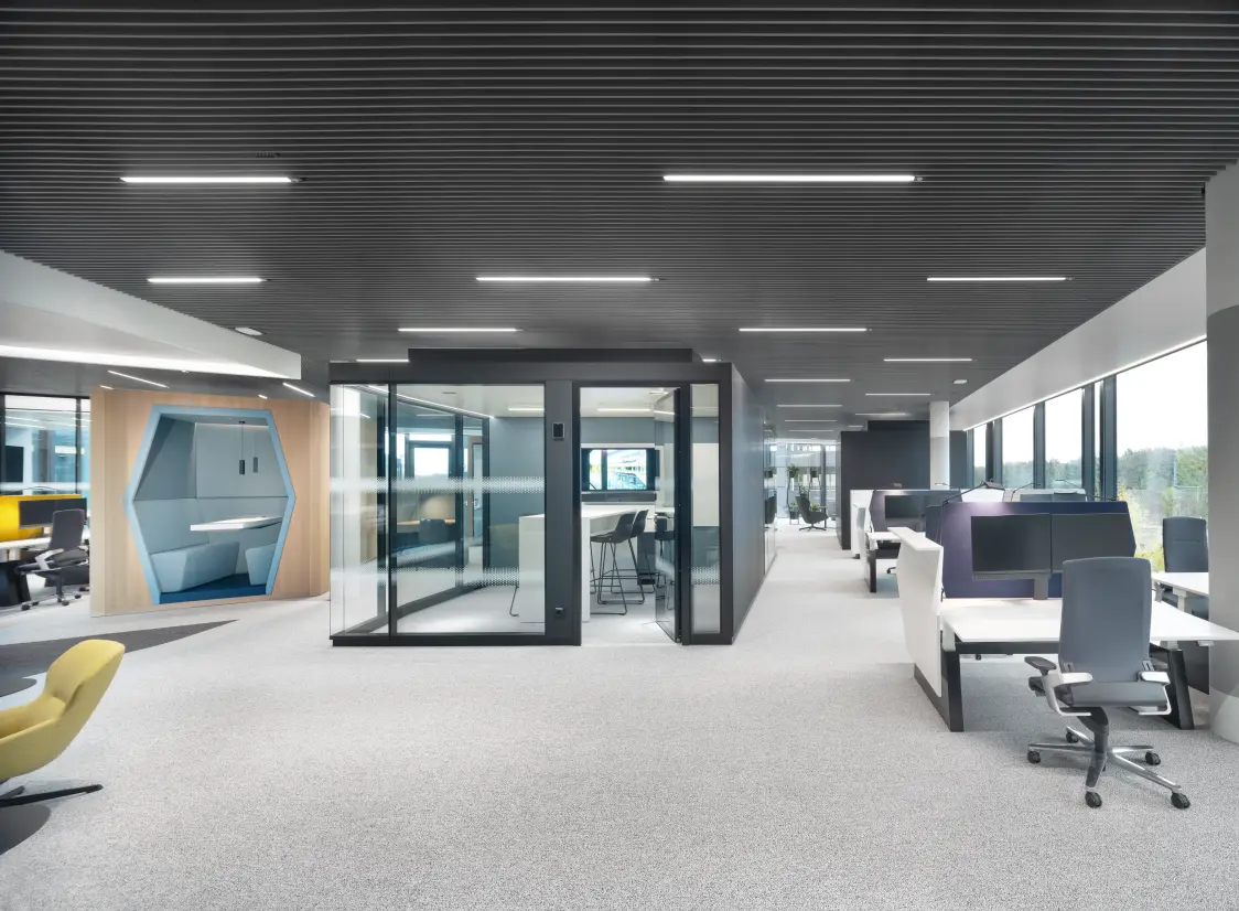 Modern open‑plan office at Continental headquarters featuring SUPERSYSTEM inline lighting, glass meeting pods, acoustic ceiling panels, and ergonomic workstations.