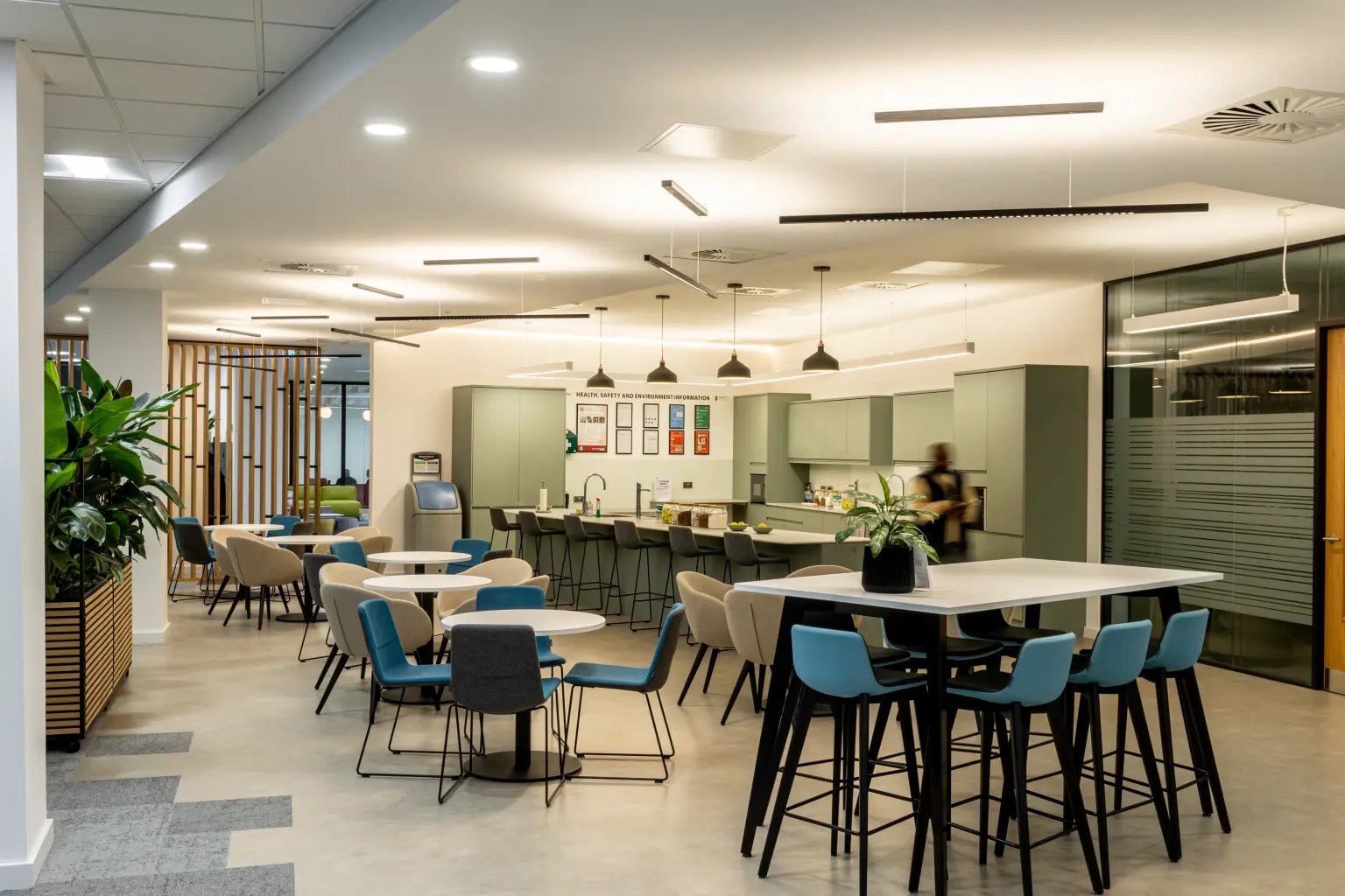 NG Bailey, White Rose Office Park - NG Bailey Headquarters, White Rose Office Park - A lady standing in a stylish breakout area with kitchenette with high tables, stylish stool seating and sleek linear lighting