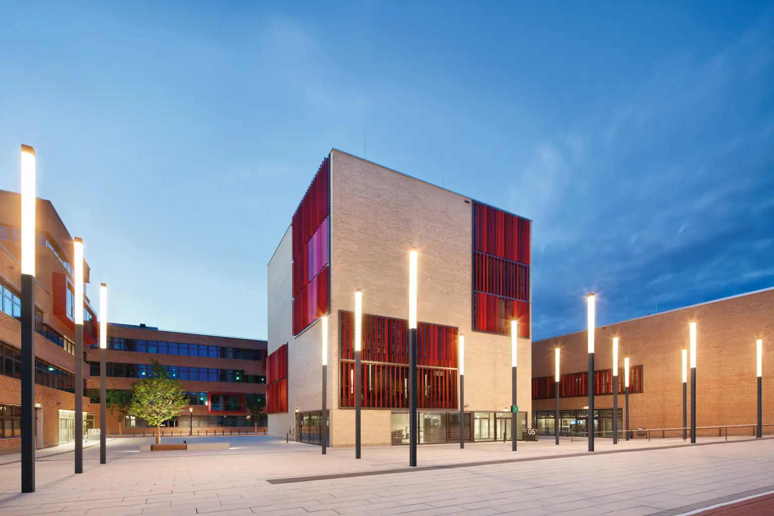 Éclairage public sur une place devant un bâtiment aux grandes fenêtres rouges