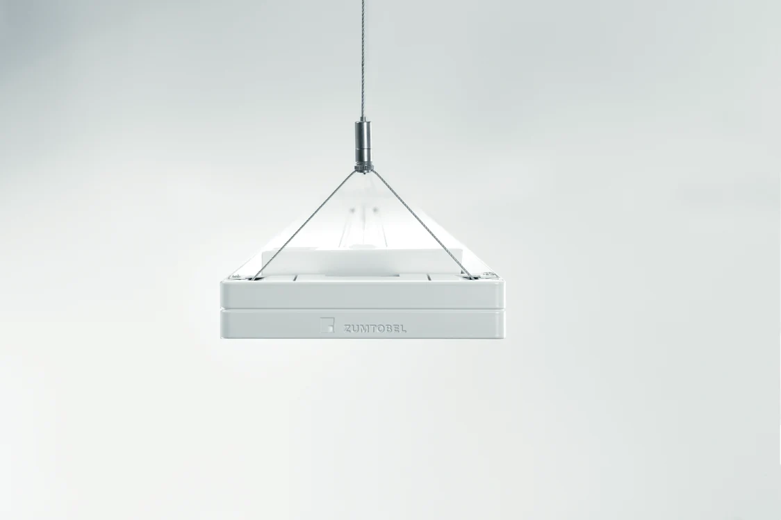 Das CLARIS-Beleuchtungssystem von Zumtobel hängt an Drahtseilen und bietet eine minimalistische Ästhetik mit klaren Linien in einem neutralen Raum.